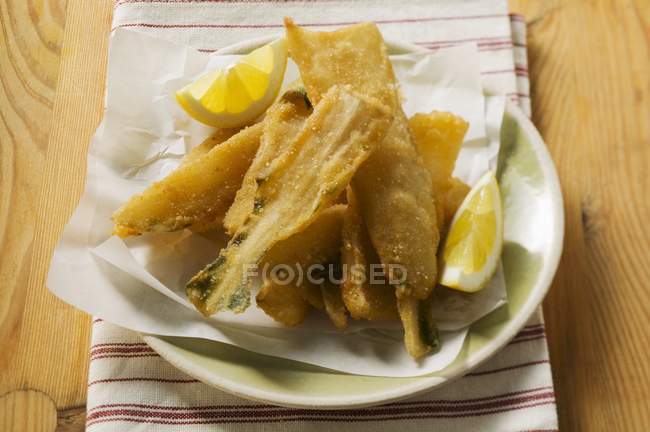 Tallos de acelga empanados con cuñas de limón en plato blanco con papel - foto de stock