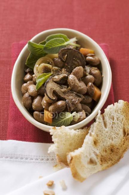 Stewed beans with ceps in small white bowl over red surface — Stock Photo