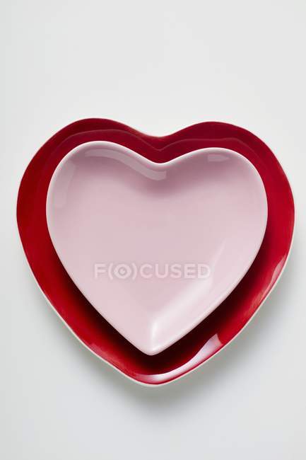 Primer plano vista superior de las placas en forma de corazón rojas y rosadas en la superficie blanca - foto de stock