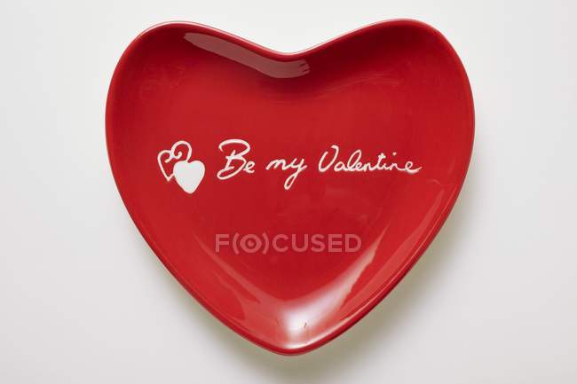 Primer plano vista superior de plato rojo en forma de corazón con las palabras Sé mi San Valentín - foto de stock
