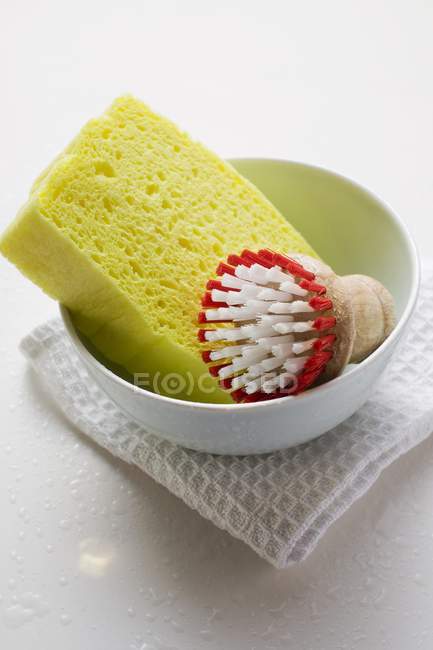 Closeup view of brush and yellow sponge in bowl on tea towel — Stock Photo