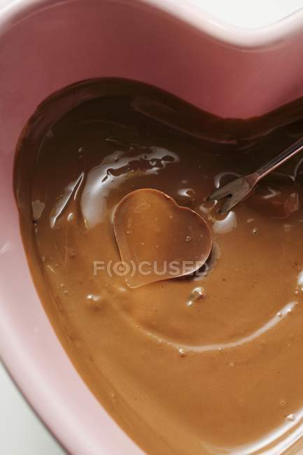 Closeup view of chocolate fondue with heart-shaped candy on fondue fork — Stock Photo