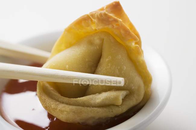 Closeup view of dipping a deep-fried Wonton in sweet and sour sauce — Stock Photo