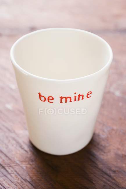 Closeup view of white beaker with the words Be mine on wooden surface — Stock Photo