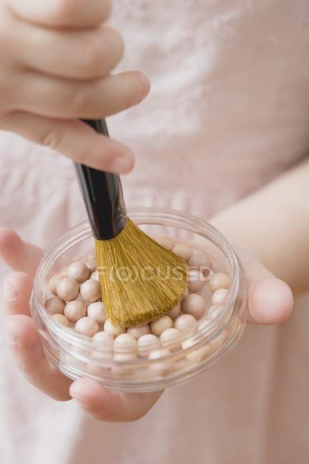 Primer plano vista recortada de niña sosteniendo perlas en polvo y cepillo - foto de stock