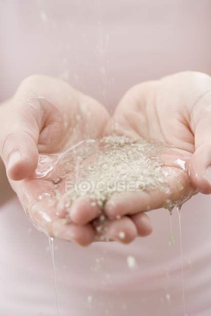 Vue rapprochée de l'écoulement de l'eau sur les mains femelles avec des granules — Photo de stock