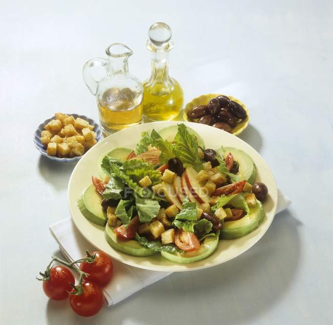 Салат авокадо с яблочными ломтиками и чесночными гренками на белой тарелке поверх полотенца на белом фоне — стоковое фото