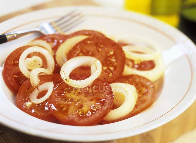Ensalada de tomate y cebolla en plato blanco con tenedor - foto de stock
