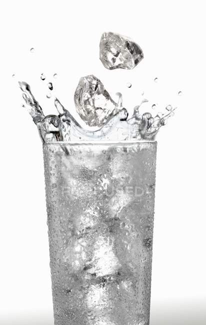 Ice cubes falling into glass of water — Stock Photo