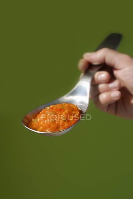 Human hand holding Pepper chutney on spoon on green background — Stock Photo