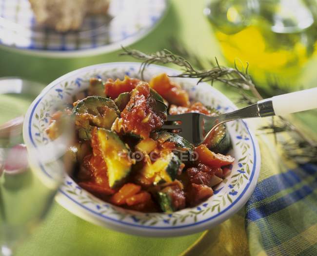 Courgette and tomato ragout with onion, garlic and rosemary on plate with fork — Stock Photo
