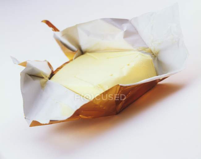 Vista de primer plano de la mantequilla en el envoltorio de papel sobre la superficie blanca - foto de stock