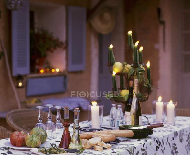 Tomatoes, baguette, oil, vinegar and candles on table outdoors — Stock Photo