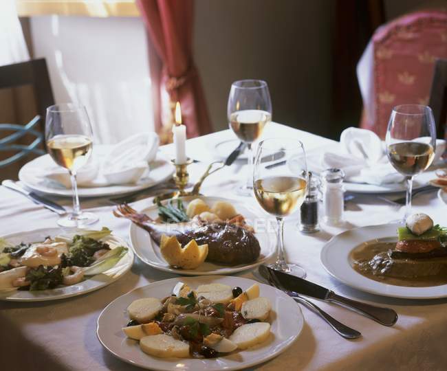 Vista de primer plano de aperitivos con vino blanco y plato de pescado en la mesa puesta - foto de stock