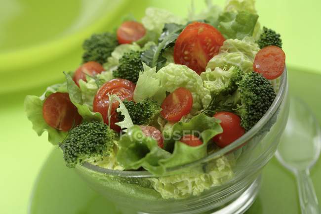 Salat mit Brokkoli und Cocktailtomaten in Glasschüssel über grüner Oberfläche — Stockfoto