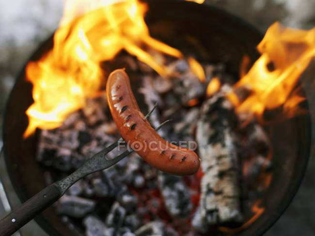 Closeup view of a sausage on a fork over fire — Stock Photo