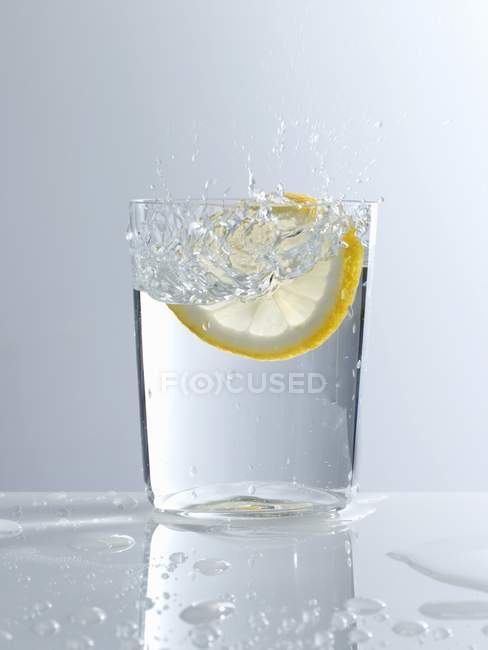 Падение ломтика лимона в стакан воды — стоковое фото