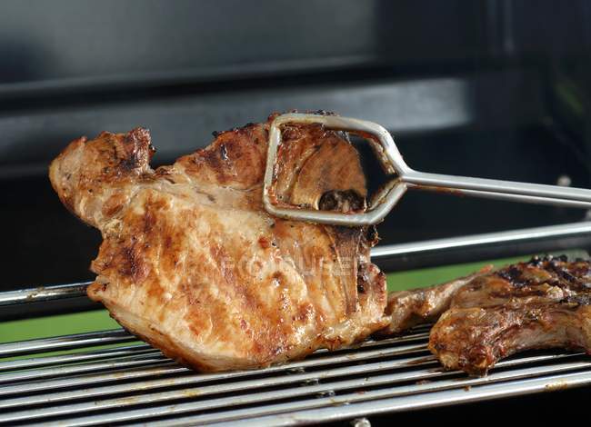 Turning pork chop with grill tongs — Stock Photo