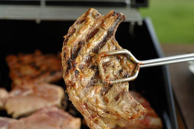 Lamb chop in grill tongs — Stock Photo
