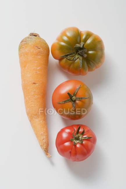 Une carotte et trois tomates — Photo de stock