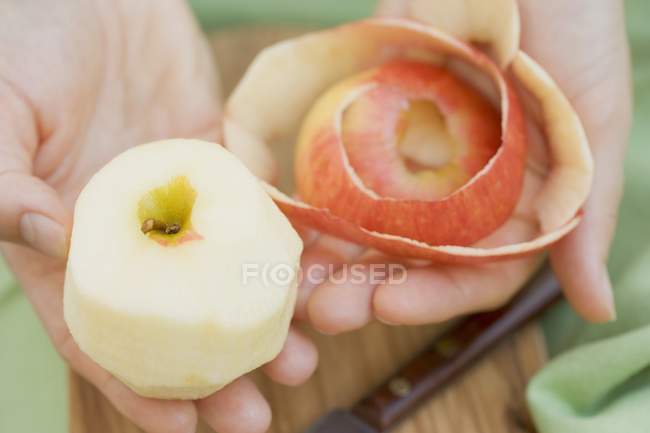 Mãos segurando maçã descascada e casca — Fotografia de Stock