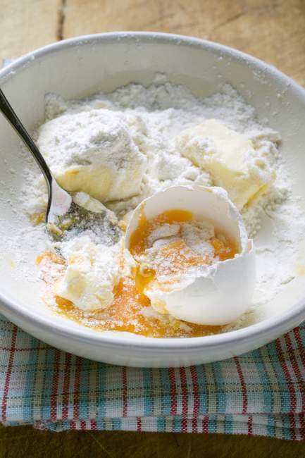Vista close-up de farinha com ovo quebrado e manteiga na tigela — Fotografia de Stock