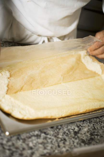 Ausgeschnittene Ansicht eines Kochs, der Backpapier vom Biskuitboden zieht — Stockfoto