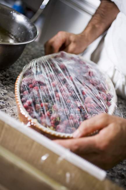 Closeup cropped view of person covering berry dessert with cling film — Stock Photo
