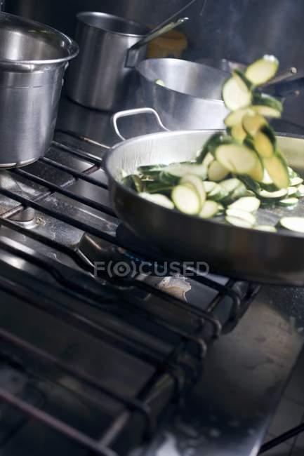 Tossing courgette slices in frying pan at kitchen — Stock Photo
