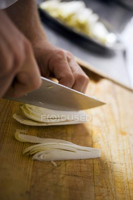 Slicing chicory with knife in hands over wooden desk — Stock Photo