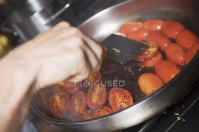 Hand Turning tomatoes in frying pan at kitchen — Stock Photo