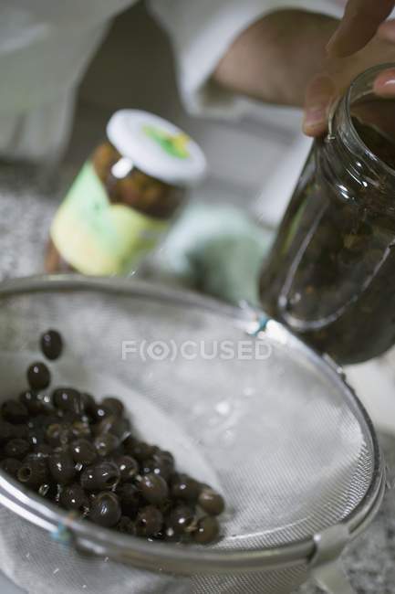 Drenando azeitonas pretas em uma peneira — Fotografia de Stock