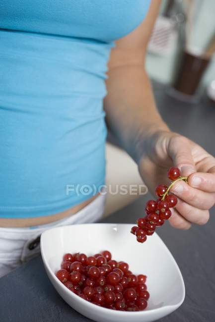 Woman taking redcurrants out of bowl — Stock Photo