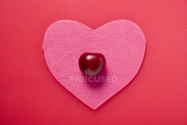Cherry on pink fabric heart — Stock Photo