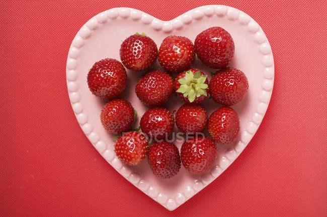 Fresas en plato rosa en forma de corazón - foto de stock