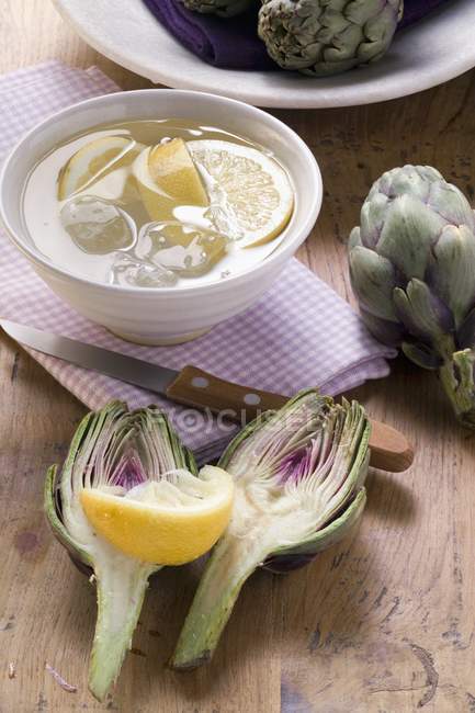 Artichokes with lemon water in bowl — Stock Photo