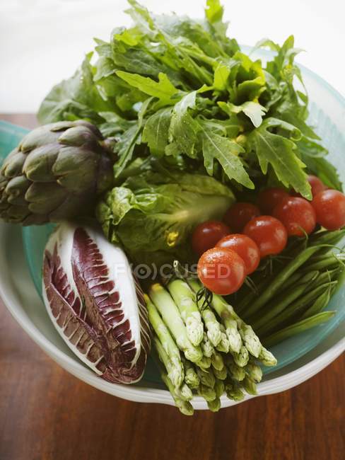 Свежие овощи в пластиковой тарелке над деревянной поверхностью — стоковое фото
