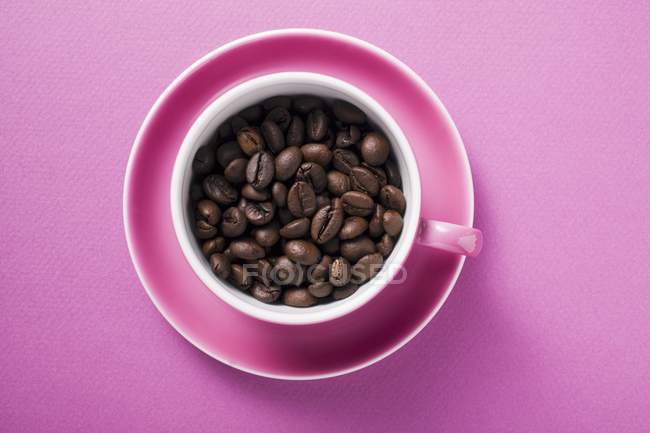 Кофейные зерна в розовой чашке кофе — стоковое фото