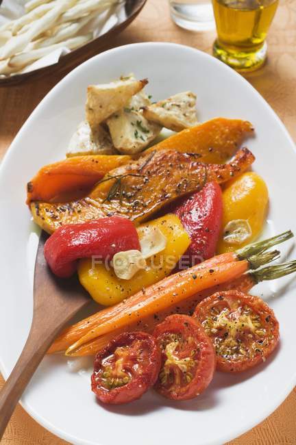 Roasted vegetables on white platter with wooden spoon — Stock Photo