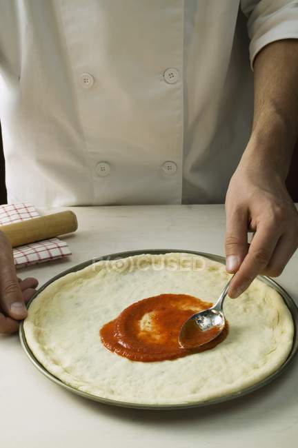 Chef extendiendo pizza con salsa - foto de stock