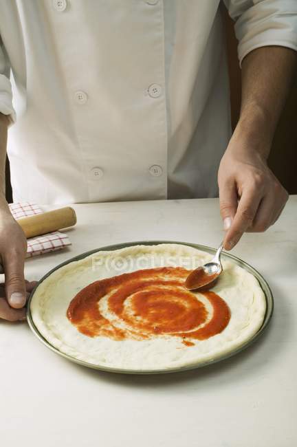 Chef extendiendo pizza con salsa - foto de stock