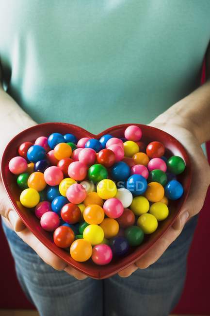 Cropped view of person holding heart-shaped dish of bubble gum balls — Stock Photo