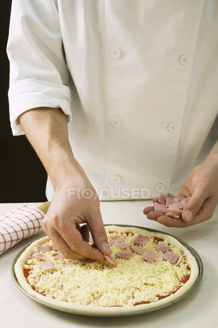 Chef topping pizza with ham — Stock Photo