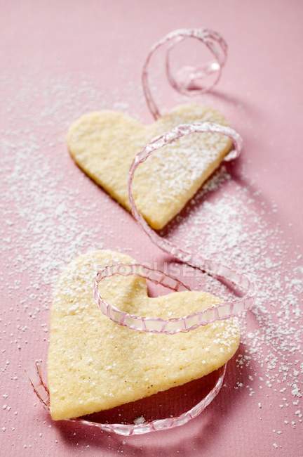 Vista close-up de corações de pastelaria com açúcar de confeiteiro e fita rosa — Fotografia de Stock