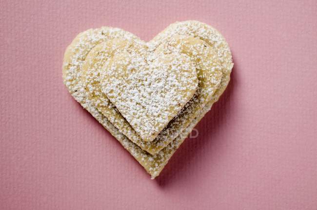 Vista close-up de corações de pastelaria empilhados com açúcar de confeiteiro na superfície rosa — Fotografia de Stock