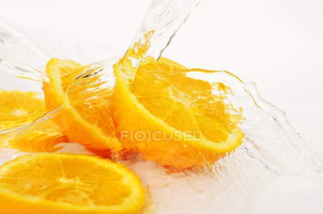 Оранжевые ломтики с брызгами воды — стоковое фото