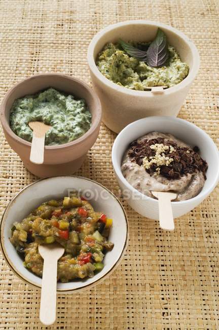 Elevated view of four different spreads with spoons in bowls — Stock Photo