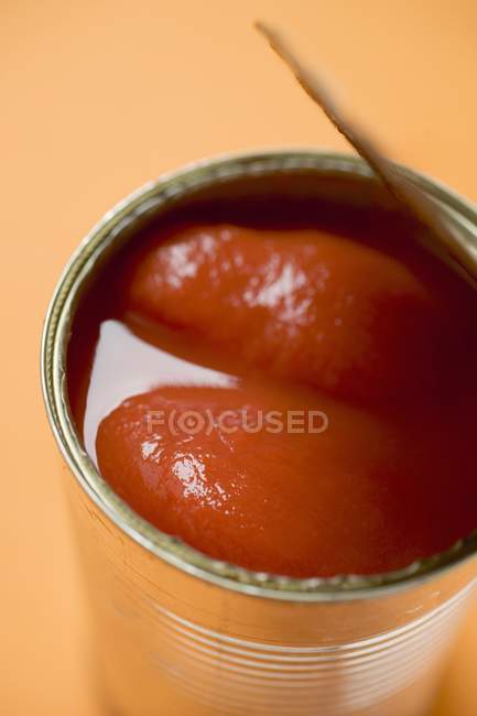 Tinned tomatoes on orange background — Stock Photo