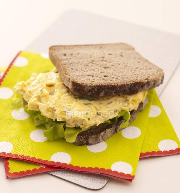Sandwich de huevo revuelto en servilletas sobre tabla de cortar - foto de stock
