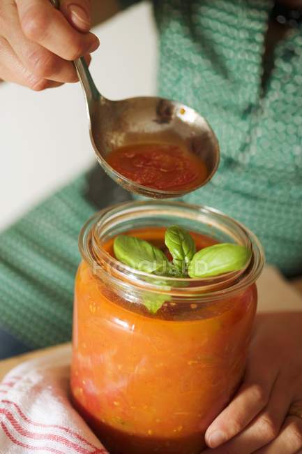 Femme tenant pot de conservation de sauce tomate et louche dans les mains — Photo de stock
